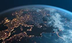 Eine Nahaufnahme der Erde aus dem Weltraum, die Europa und Teile Asiens zeigt. Die Kontinente sind mit vielen Lichtern beleuchtet, die Städte darstellen, während der Rest des Bildes in Dunkelheit gehüllt ist. Der Hintergrund ist ein sanftes Blau.